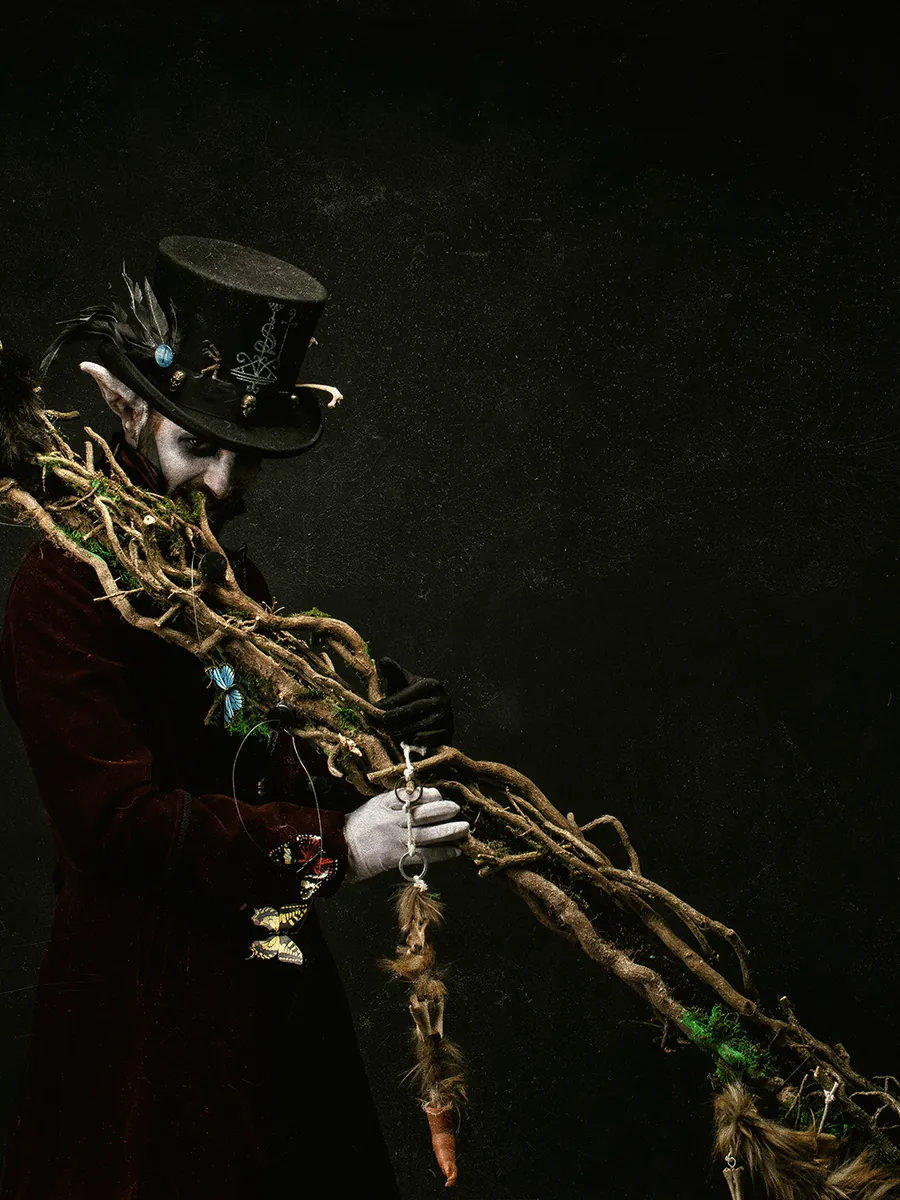 Un Lutin Samedi en haut-de-forme, le visage peint en tête de mort, brandit un bouquet de branches